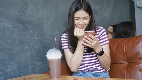 Smiling young woman holding smart phone while standing by laptop