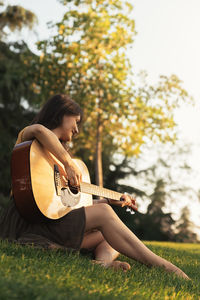 Young woman playing guitar on field