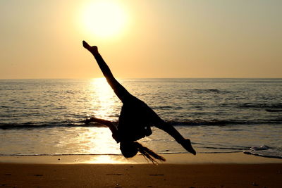 Silhouette woman jumping on sand at beach during sunset