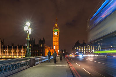 Blurred motion of double-decker bus on street by illuminated big ben against sky at night