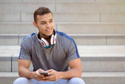 Portrait of smiling young man using mobile phone while sitting on staircase