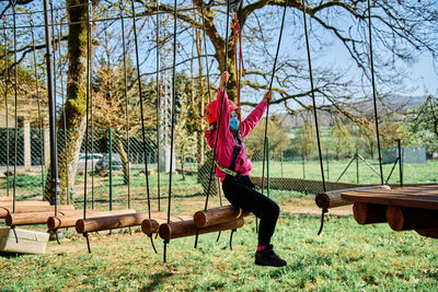 Little girl with protections practicing climbing between trees with ropes and nets