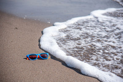 Colored sunglasses abandoned on the sandy beach by the seaside, lapped by the waves.