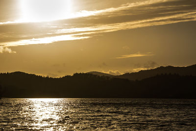 Scenic view of river by silhouette mountains against sky during sunset