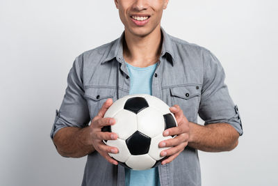 Young man holding ball while standing against gray background