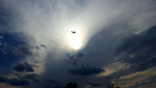 Low angle view of silhouette plane flying against cloudy sky