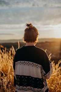 Rear view of woman standing on field against cloudy sky during sunset