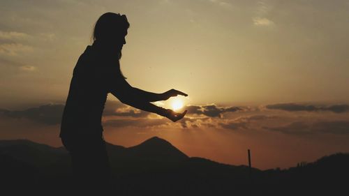 Optical illusion of silhouette woman holding sun during sunset