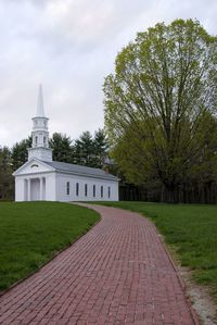 Chapel by grassy field against cloudy sky