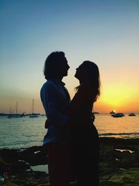 Couple standing on beach against sky during sunset