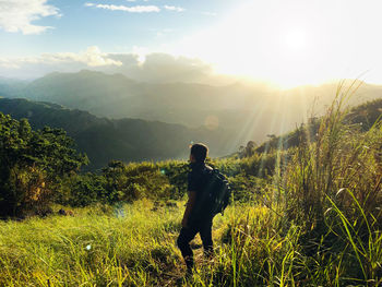 Man standing on grass while looking at mountain ranges during sunset