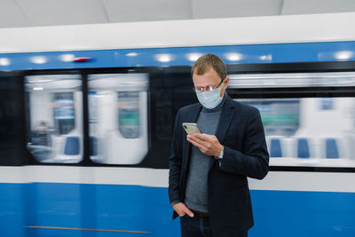 Businesswoman wearing mask using smart phone while standing against train