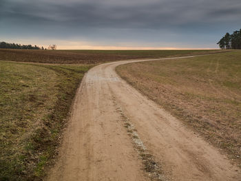 Dirt road amidst field against sky