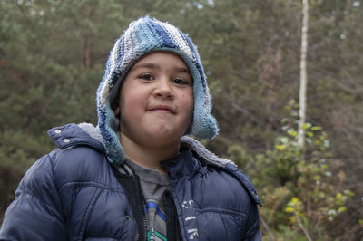 Close-up portrait of boy wearing knit hat while standing against trees