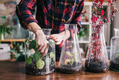 Midsection of woman planting in glass jar on table