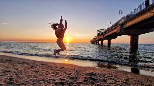 Rear view of woman standing at beach against sky during sunset