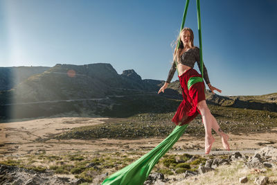 Full length of woman exercising while handing on textile against sky