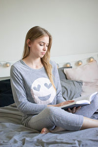 Young woman using mobile phone while sitting on bed at home