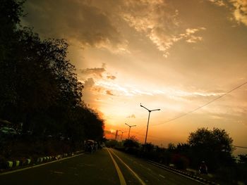 Road by trees against sky during sunset