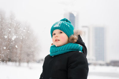 Child boy wearing a blue hat and a black coat is standing in the snow, enjoying the winter weather