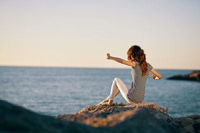 Woman on rock by sea against sky during sunset