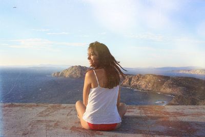 Rear view of woman sitting on cliff against sea