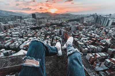 Low section of man with cityscape against sky during sunset