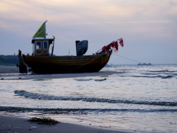 Boat moored on beach against sky during sunset