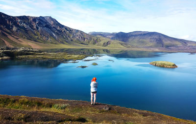 Rear view of man standing by lake against sky