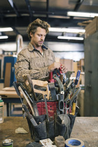 Carpenter standing by tool belt on table in workshop