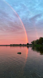 Scenic view of rainbow over lake against sky during sunset