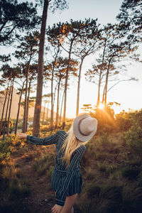 Young woman wearing hat in forest against sky at sunset