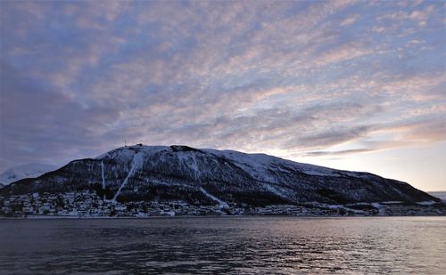 Scenic view of sea by snowcapped mountains against sky during sunset