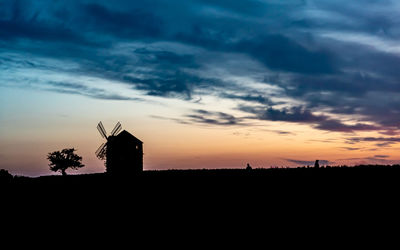 Silhouette cross on landscape against sky during sunset