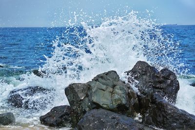 Waves splashing on rocks at shore against sky