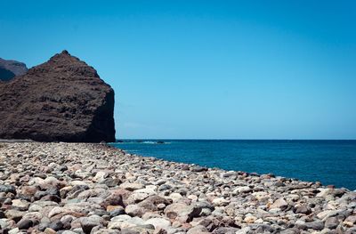 Rocks by sea against clear blue sky