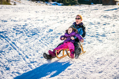 Mother and daughter tobogganing on snow