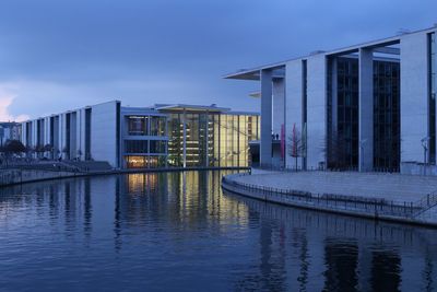 Buildings by lake against sky at dusk