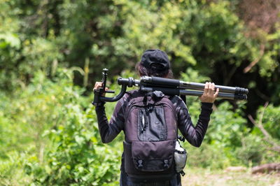 Rear view of woman carrying tripods in forest