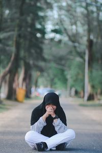 Portrait of young woman wearing hijab sitting on road