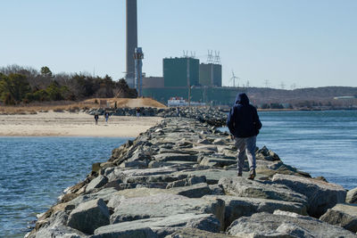 Rear view of man on rock by sea against clear sky