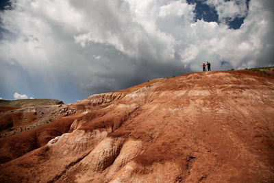 A man and a woman on the top of the red mountain against the sky