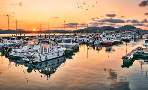 Boats moored in harbor at sunset