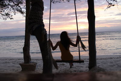 Woman sitting on beach against sky during sunset
