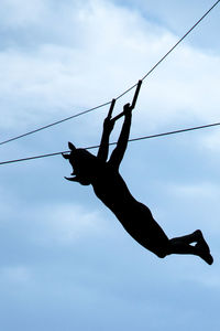 Low angle view of silhouette man performing stunt on rope against clear sky