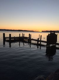 Silhouette wooden posts in sea against clear sky during sunset