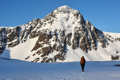 Rear view of person walking on snow covered mountain against sky