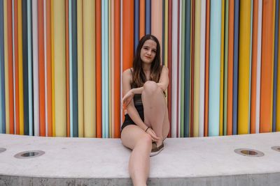 Full length portrait of woman sitting against wall