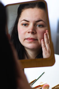 Vertical image of millennial caucasian woman doing self make up applying face cream