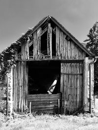 Old wooden cottage by house against sky, black and white